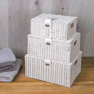 Set of three white wicker storage baskets with lids on a wooden surface.