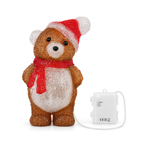 A glittery teddy bear Christmas ornament wearing a red and white Santa hat and red scarf, shown standing next to its white battery pack with a clear cord on a white background.