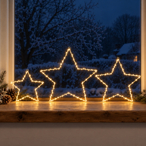 Three large star-shaped Christmas light decorations outlined with warm white lights, displayed on a wooden windowsill with a snowy outdoor view in the background.