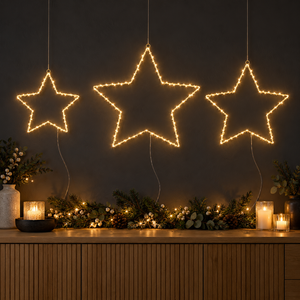 Set of three warm white LED Christmas stars hanging above a festive garland and candles.