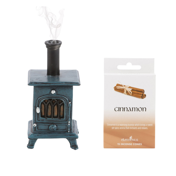 A miniature dark teal wood-burning stove incense holder with a black chimney and rising smoke, shown next to its white and beige 'cinnamon' scented packaging card by Elemes.