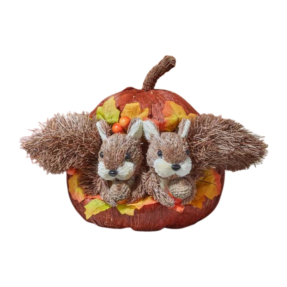 A decorative autumn centerpiece featuring two plush brown squirrel figures nestled inside a wrapped orange pumpkin, surrounded by faux fall leaves and small berries, displayed on a wooden surface.