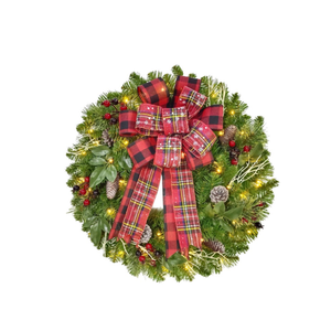 An artificial Christmas wreath with green pine branches, warm white string lights, pinecones, red berries, and a large red plaid bow with white snowflake details, isolated on a white background.
