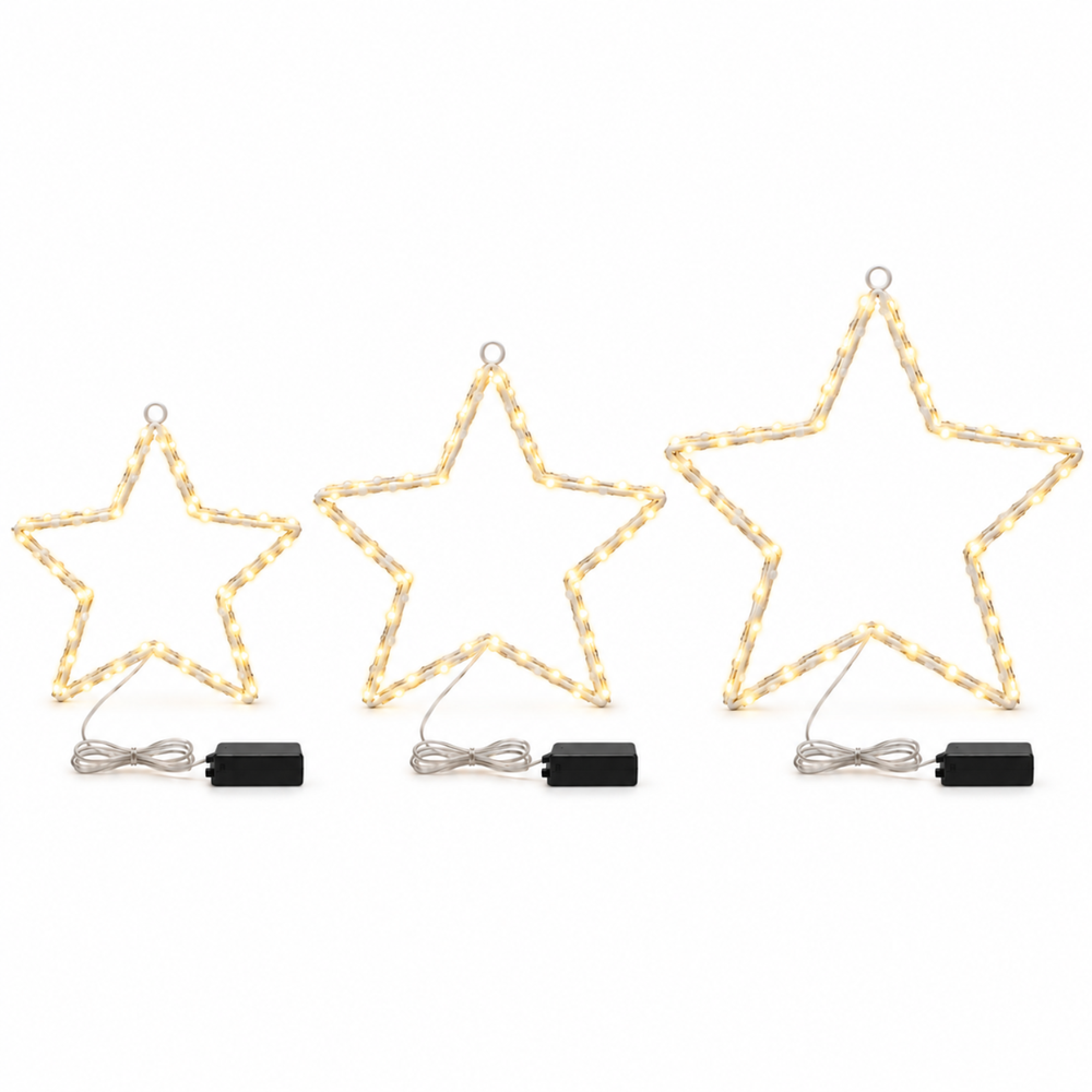 Three large star-shaped Christmas string lights glowing warm yellow on a white windowsill, with a snowy outdoor scene visible in the background and candles on both sides.