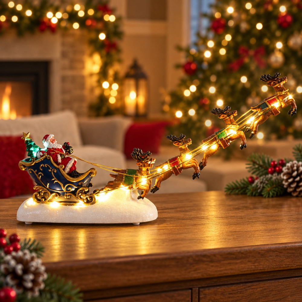 A festive Christmas ornament shaped like Santa's sleigh being pulled by reindeer, displayed on a wooden table in a cozy living room with a blurred Christmas tree and fireplace in the background.