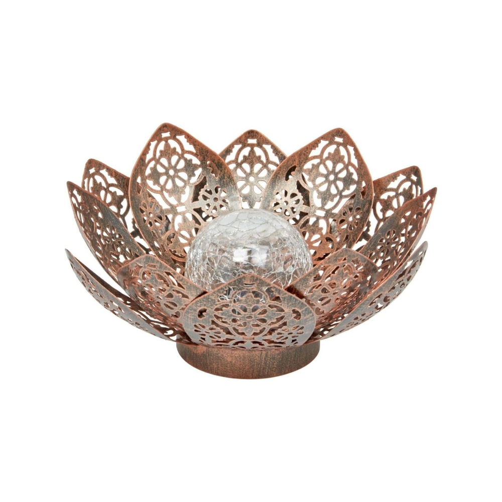 A bronze-colored metal lantern in a lotus flower shape with a crackled glass globe light, illuminated and placed on a stone surface with flowers in the background.