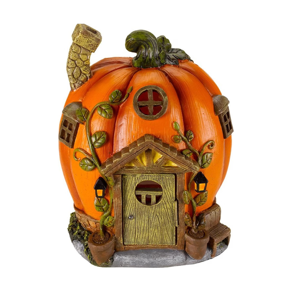A decorative pumpkin-shaped house night light with a glowing warm yellow interior, detailed door, windows, vine accents, and small lanterns, shown outdoors against a dark foliage background.