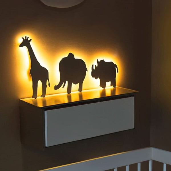 Silhouettes of a giraffe, elephant, and rhino on a wall with warm light