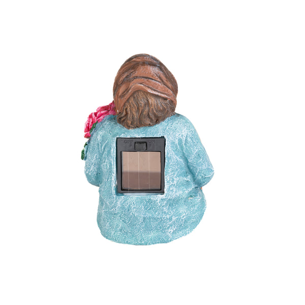 A garden statue of a woman with brown hair, wearing a textured light blue dress, shown from the back. A rectangular solar panel is mounted on the back of the statue.