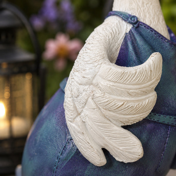 A close-up of a white winged hand sculpture or ornament attached to a blue fabric-covered support, with a blurred outdoor background and a lantern on the left.