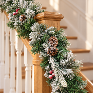 A festive Christmas garland draped over a wooden staircase railing, featuring flocked green pine branches, pinecones, and small red berries.