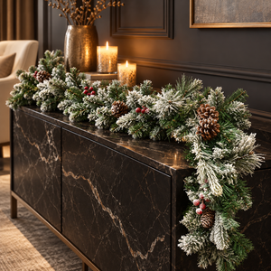 Frosted green pine garland with brown pinecones and small red berries draped across a black marble sideboard in a dark, elegantly decorated room.