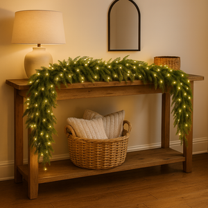 Wooden console table with festive garland and lights, basket with pillows, and lamp in a warm setting.