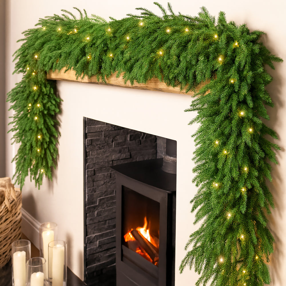 Decorative green garland with lights on a fireplace mantel.