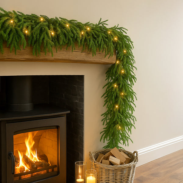Fireplace with greenery and lights on a mantel, candles, and firewood basket.