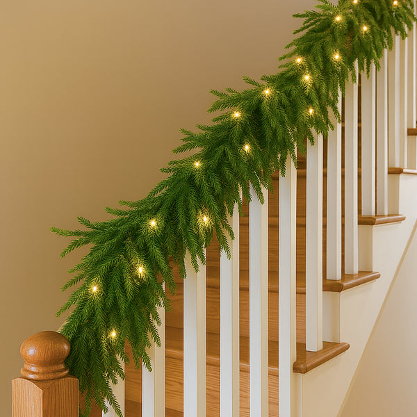 Green Christmas garland with lights on a staircase railing against a beige wall.