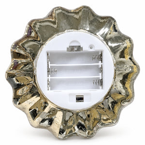 The back view of a scalloped, metallic silver decorative night light with a white battery compartment and a sliding switch button