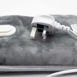 Close-up of a gray heated towel or blanket pad with a white UK two-pin power plug and cord, shown on a white background.