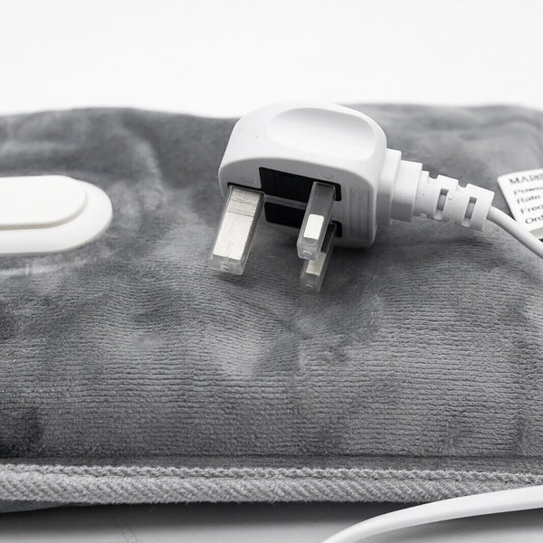Close-up of a gray heated towel or blanket pad with a white UK two-pin power plug and cord, shown on a white background.