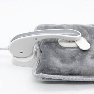 A white handheld steam iron placed on top of a gray heated blanket or pad, photographed on a clean white studio background.