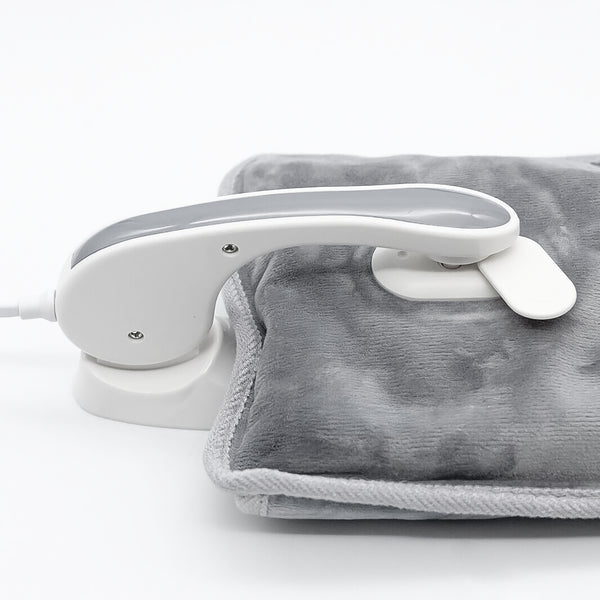 A white handheld steam iron placed on top of a gray heated blanket or pad, photographed on a clean white studio background.