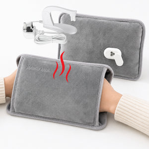 Gray heated wrist wrap shown being worn on a person's wrist, with a second wrap and a white power adapter in the background. Red wavy lines indicate heat.