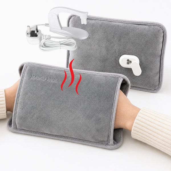 Gray heated wrist wrap shown being worn on a person's wrist, with a second wrap and a white power adapter in the background. Red wavy lines indicate heat.