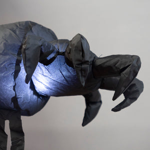 A close-up of a black fabric insect puppet with articulated legs and mandibular claws, shown against a plain light gray background.