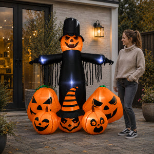 A woman stands beside a large Halloween inflatable decoration featuring a black scarecrow-like figure with glowing blue hands and multiple orange jack-o'-lantern pumpkins, set in front of a house patio at dusk.