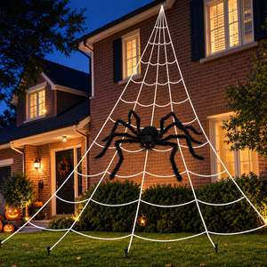 A large black spider decoration hanging from a white web-like Halloween yard display on the front lawn of a brick house at dusk.