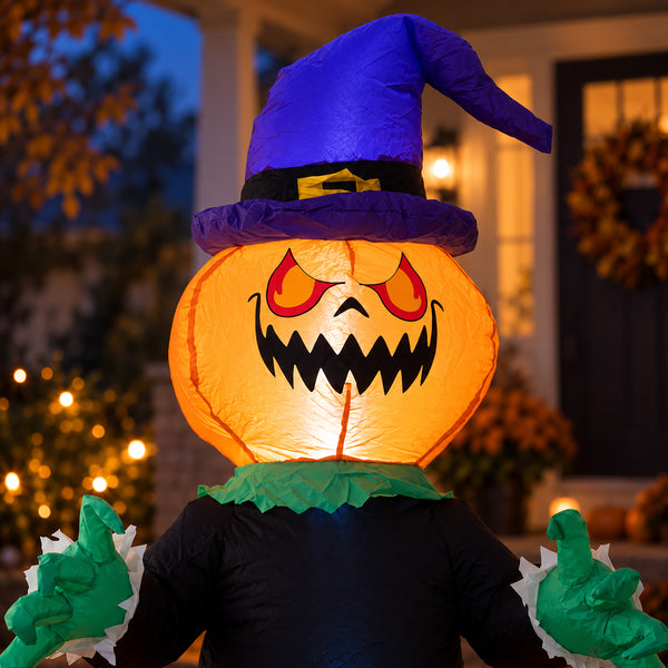 A large inflatable Halloween decoration shaped like a witch's character, featuring a glowing orange jack-o'-lantern head with red eyes and a wide black grin, a purple witch hat, green gloves, and a black body, photographed outdoors in front of a house at dusk.