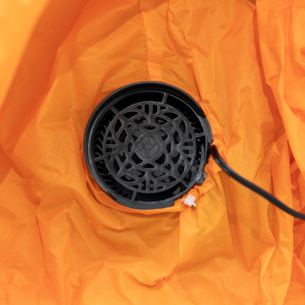 Close-up of a black circular vent or fan component attached to bright orange fabric with a black cord extending to the right.