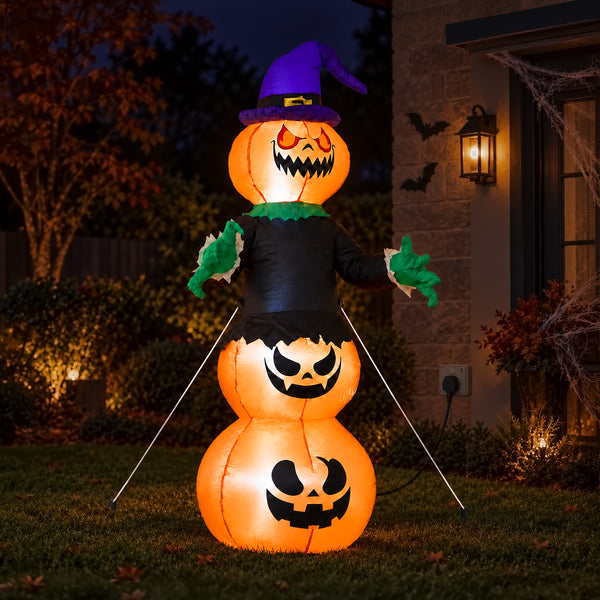 A large inflatable Halloween snowman decoration stands on a lawn in front of a house at night. The snowman is made of three glowing orange jack-o'-lantern shapes, wears a purple witch hat, a black outfit, and green gloves, with thin support poles extending outward.