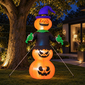 An inflatable Halloween yard decoration shaped like a witch jack-o'-lantern, standing on grass in front of a house at night. The figure has three stacked glowing orange pumpkin bodies, a purple witch hat, a black dress, green gloves, and green collar details.