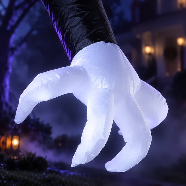 A large inflatable Halloween yard sign shaped like a clawed hand, with a black sleeve and glowing white fingers, photographed outdoors at night in a spooky yard setting.