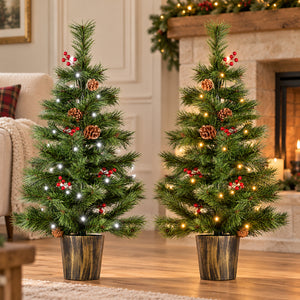 Two small artificial Christmas trees with green needles, decorated with white and warm yellow string lights, pinecones, and red berries, standing in dark wood planters on a wooden floor in a cozy living room setting.