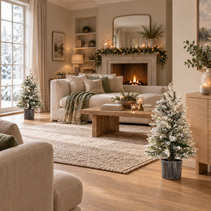 Small potted Christmas trees with snowy branches displayed around a cosy festive living room.