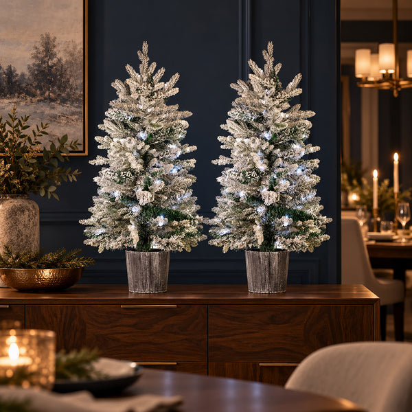 Pair of frosted Christmas trees with cool white LED lights displayed on a wooden sideboard.