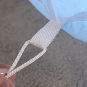 Close-up of a white woven carrying loop attached to a light blue fabric item, with a hand holding the loop against a gray textured background.