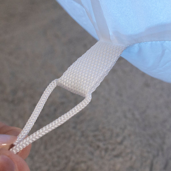 Close-up of a white woven carrying loop attached to a light blue fabric item, with a hand holding the loop against a gray textured background.
