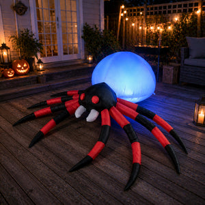 An inflatable Halloween spider decoration on a wooden deck at night, glowing with a blue orb behind it. The spider has a black head with red eyes and white fangs, and red-and-black striped legs.