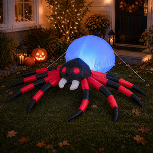 A large inflatable Halloween spider decoration with red and black striped legs, white fangs, and a glowing blue balloon on its back, displayed on a lawn in front of a house at night with lit pumpkins and holiday decor.