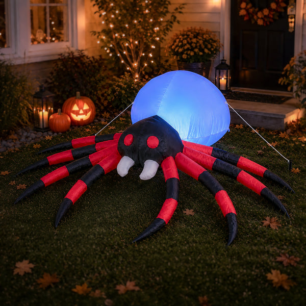 A large inflatable Halloween spider decoration with red and black striped legs, white fangs, and a glowing blue balloon on its back, displayed on a lawn in front of a house at night with lit pumpkins and holiday decor.