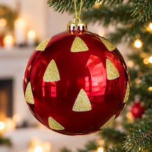 Red and gold Christmas bauble featuring glitter Christmas tree motifs hanging among festive branches.