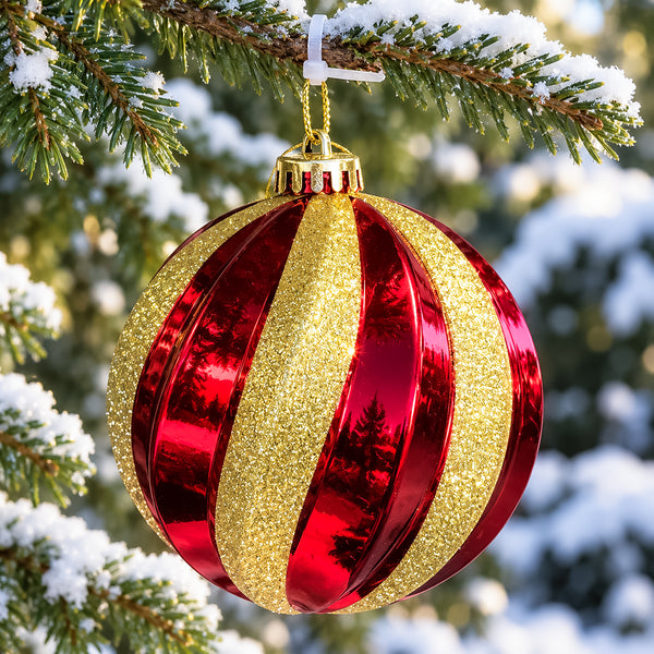 Large red Christmas bauble with curved gold glitter stripes hanging from an outdoor Christmas tree.