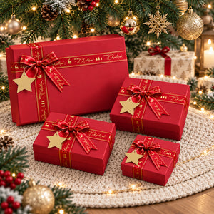 Four red Christmas gift boxes of different sizes, each tied with a red ribbon featuring gold lettering and a gold star ornament, arranged on a white crocheted rug under a decorated Christmas tree.