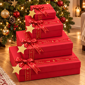 Four stacked red gift boxes with gold ribbon trim and bow, each decorated with a gold star, placed in front of a decorated Christmas tree on a wooden floor.