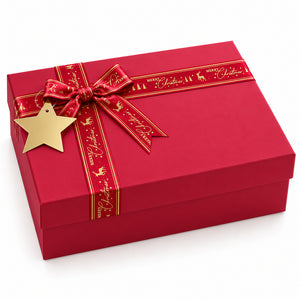 A red square gift box with a matching red ribbon tied in a bow, decorated with gold script and holiday motifs, and a gold star tag, photographed on a clean white background.