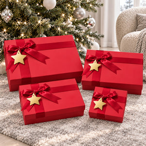Four red gift boxes of different sizes tied with red ribbons and decorated with gold star ornaments, arranged on a gray rug in front of a decorated Christmas tree.