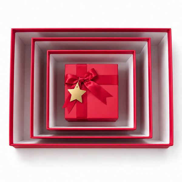 A set of nested square gift boxes in red and white, with a small red gift box tied with a red ribbon and a gold star ornament in the center, photographed from above on a white background.